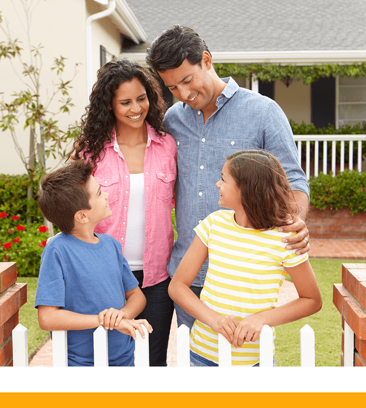 Family with two kids smiling while standing in front of their home